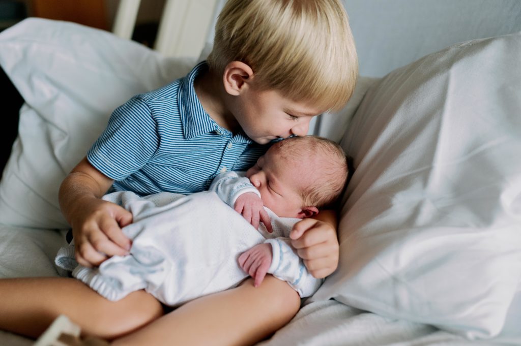 brother snuggling with newborn in hospital
