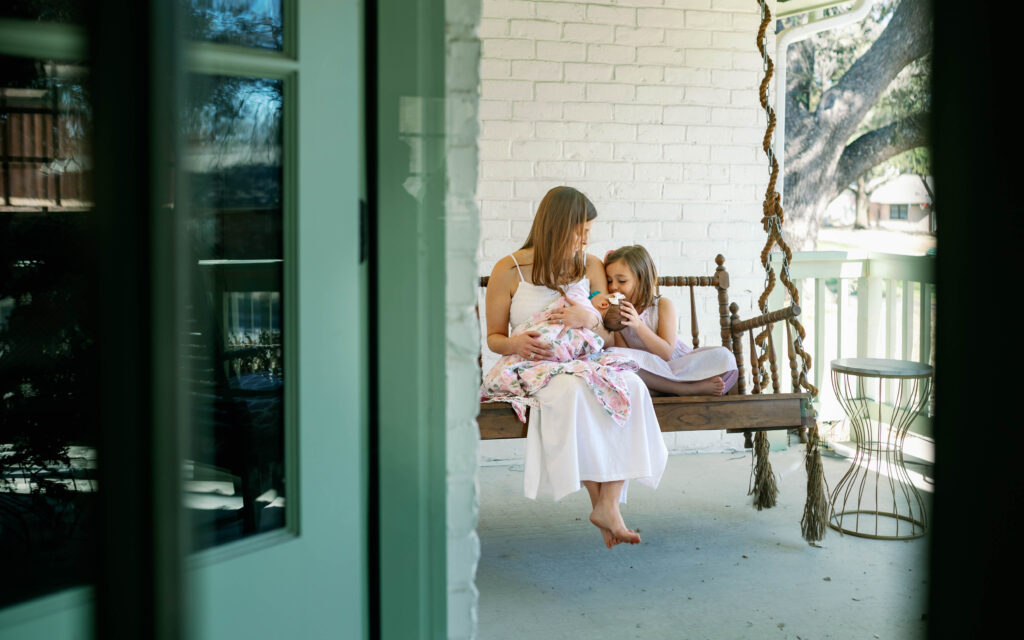mom and daughter snuggling with newborn sister on the porch