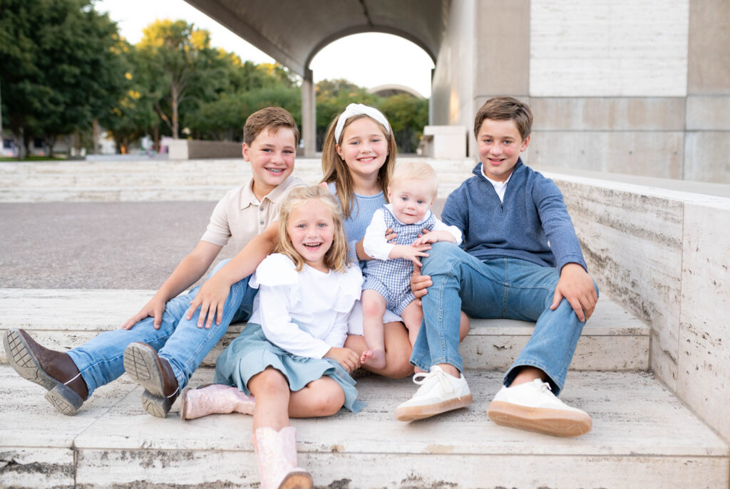Fall mini photo sessions capture a group of 5 young siblings sitting on the Kimbell steps smiling at the camera.
