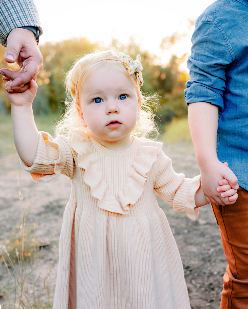 A toddler holding family hands for a family picture.
