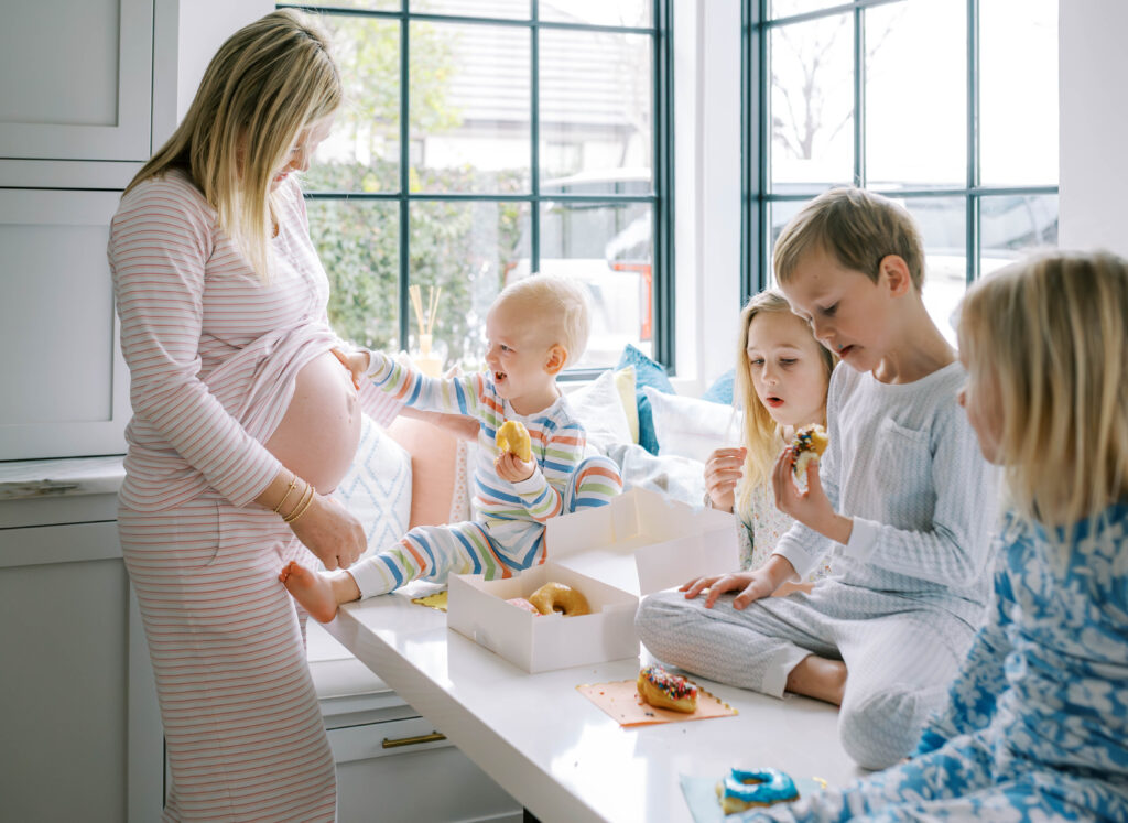 Mom is having a donut party with her children while the youngest is playing peek-a-boo with her growing baby bump.