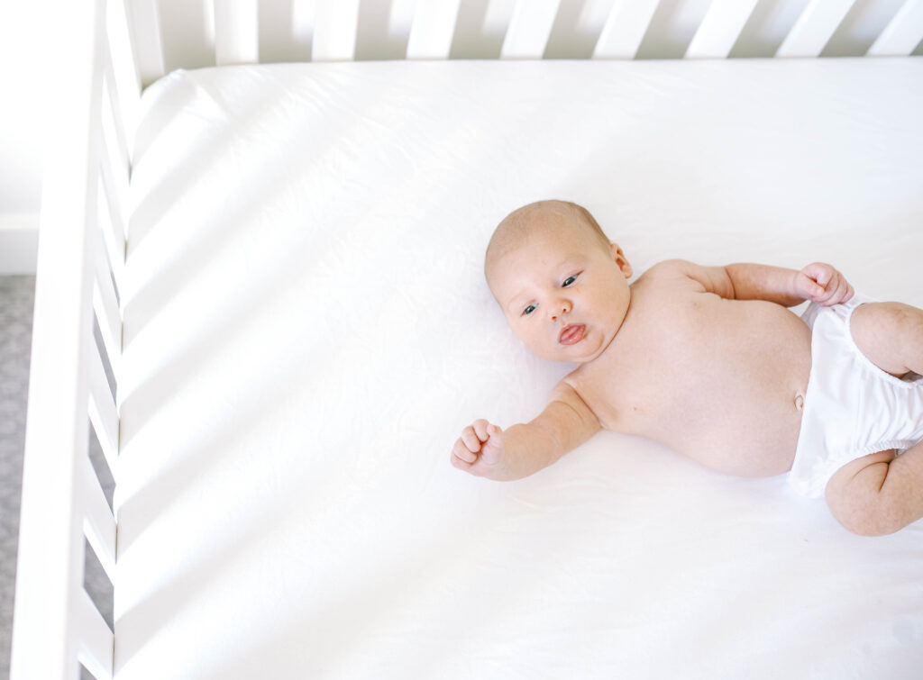 Newborn baby relaxing in crib beofre nodding off to sleep during Aledo newborn session.

