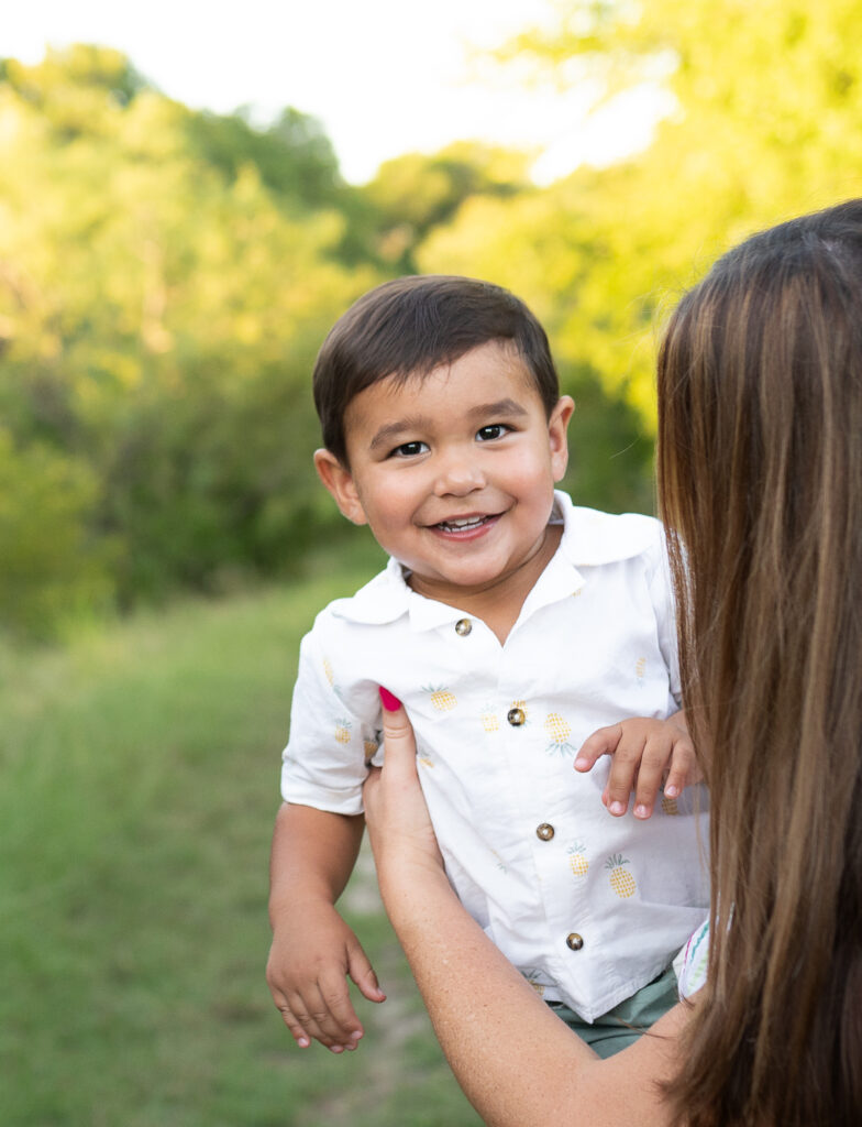 Outdoor portrait of a toddler boy while his mom is playfully holding him up.