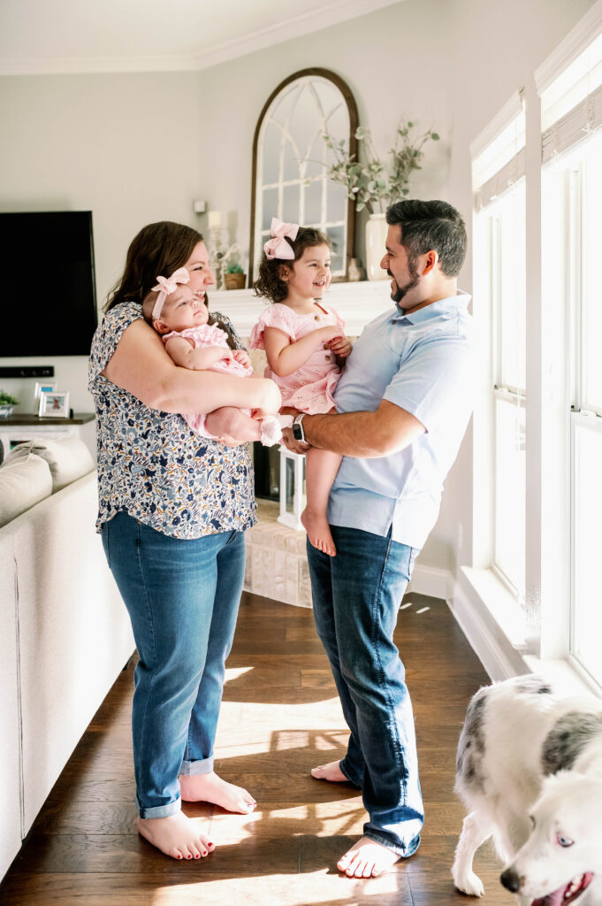A Fort Worth newborn photographer captures mom, dad, and older daughter, and newborn looking at each other in their Mansfield home.
