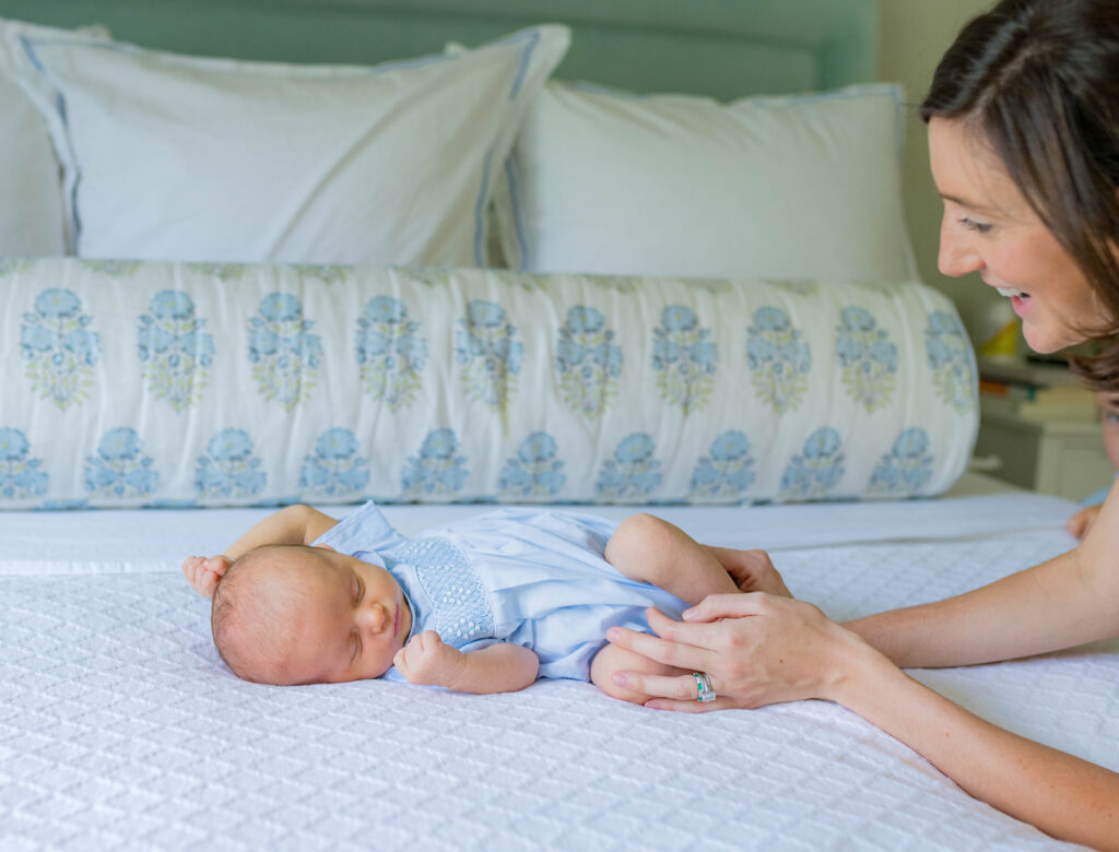  Mom is helping soothe her newborn baby, who is lying on a bed during an in-home newborn photo session.