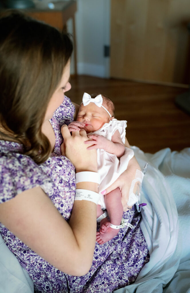Mom is sitting in the hospital bed holding and admiring her newborn daughter at Baylor All Saints Fort Worth Labor and Delivery.
