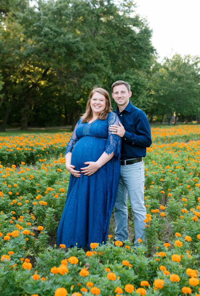 A couple stands together in a field of fall flowers during an outdoor maternity session.
