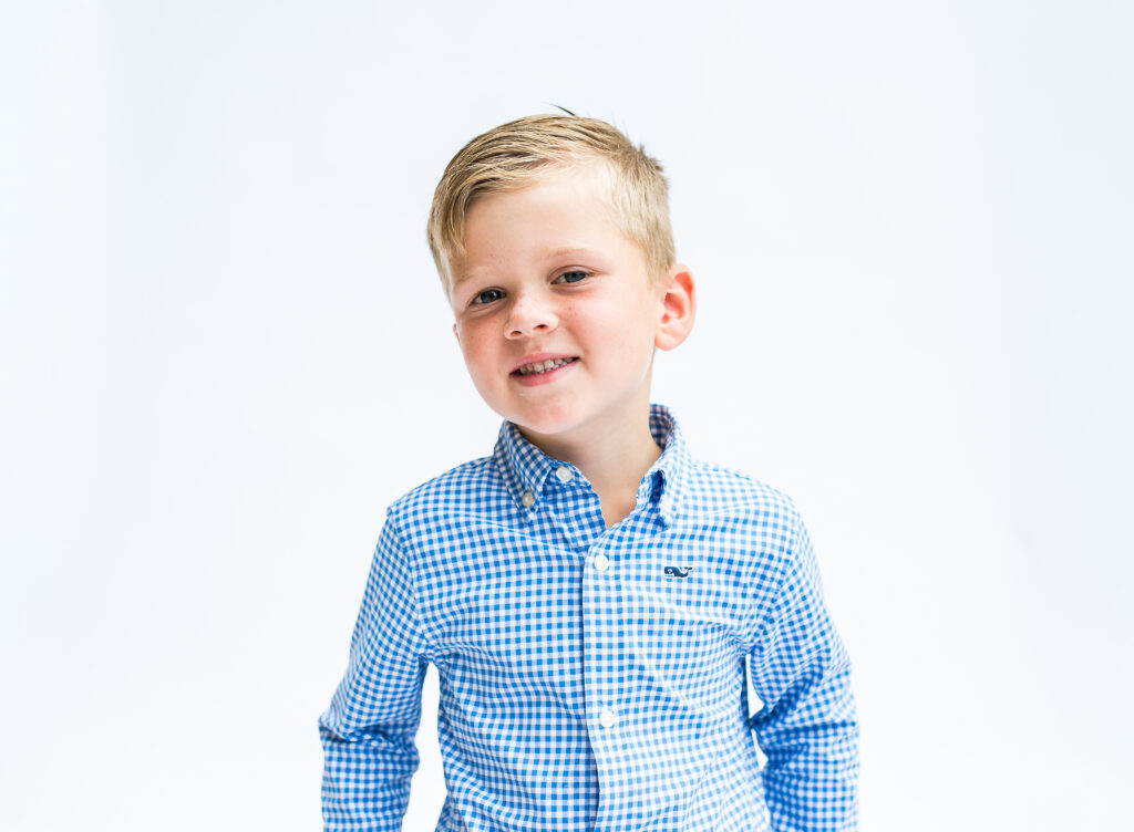A young boy casts a sideways smile at the camera while sitting for a preschool portrait session with Allison Krogness.