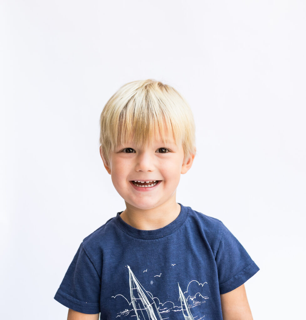Fort Worth preschool photographer captures young boy smiling at the camera with a white back drop.
