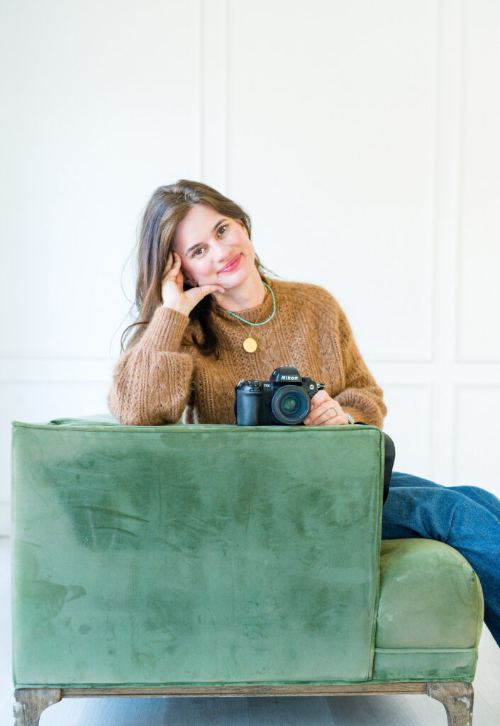 Allison Krogness is sitting on a green sofa at the Lumen Room while holding her camera.