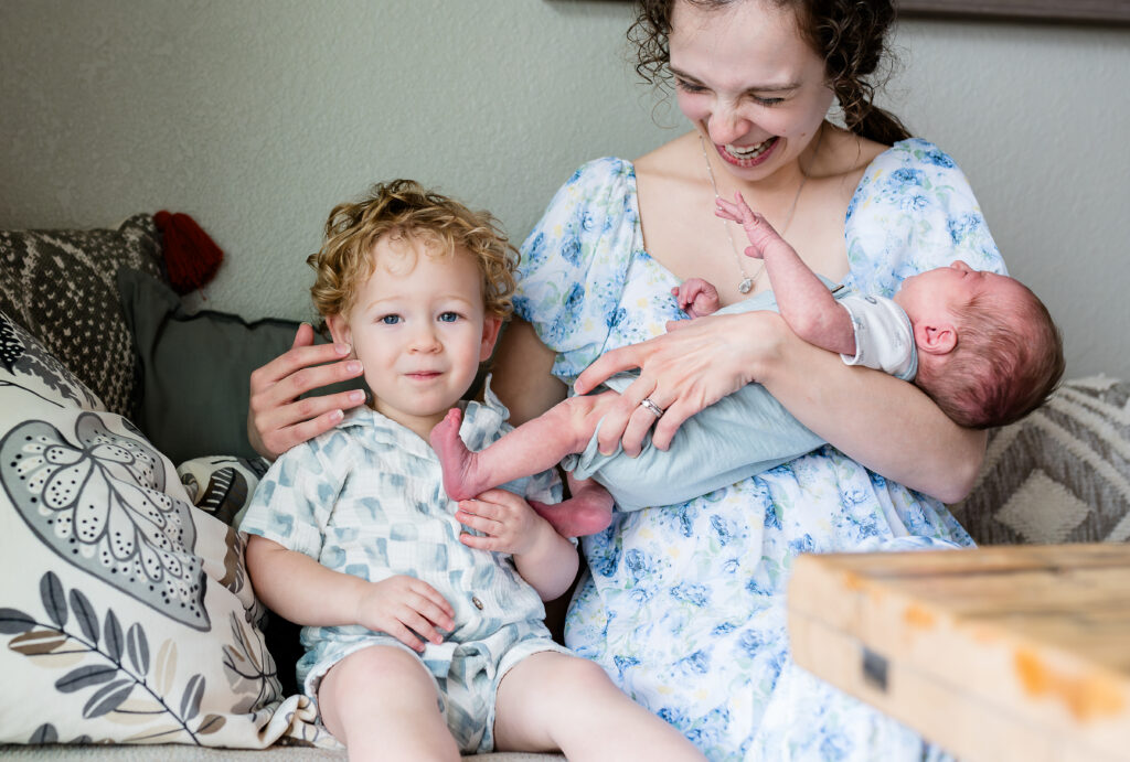 In-home newborn photos in Fort Worth capture a toddler grinning at the camera after he smells his little brother's toes.