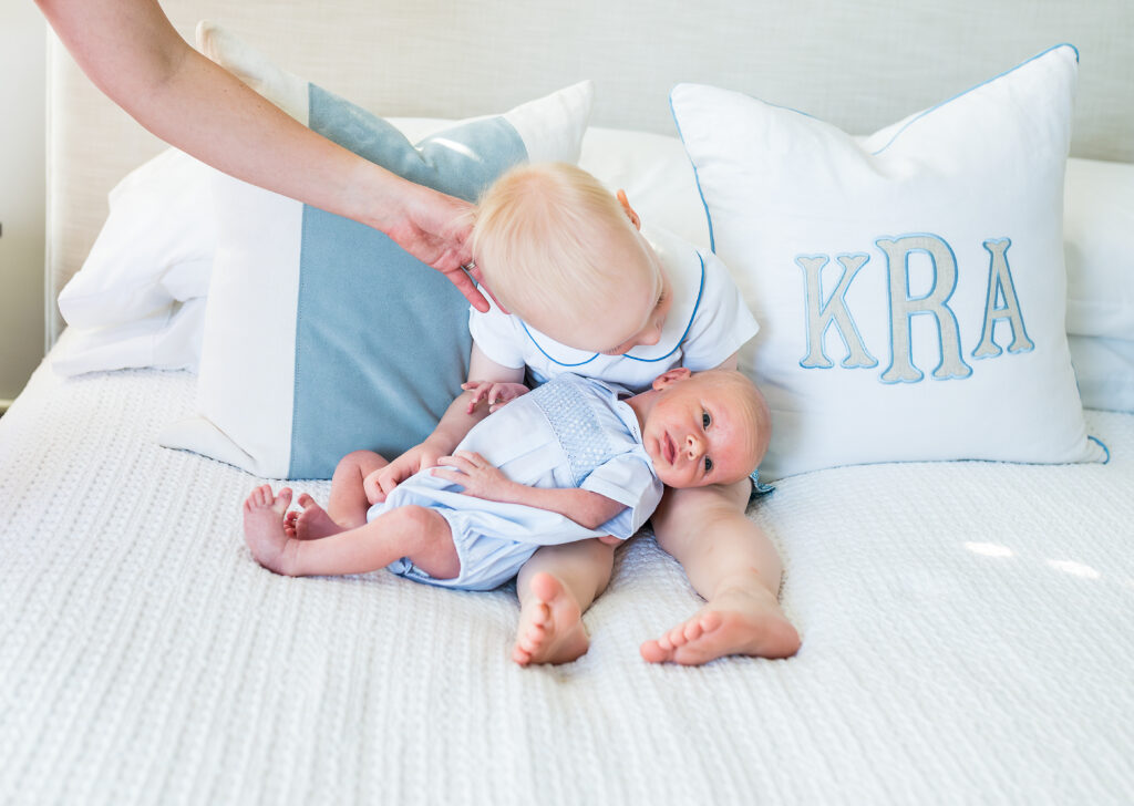 Big brother is carefully cradling his newborn brother, sitting on the parents' bed during a session with Southlake newborn photographer, Allison Krogness.
