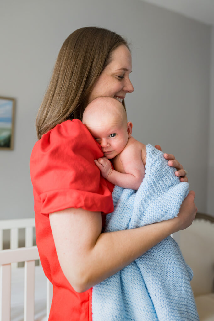 Mom is holding her newborn son against her chest while the baby is peeking out at the camera during an in-home Southlake newborn photo session.
