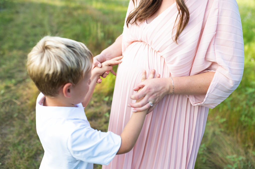 A son places his hands on his mother's pregnant belly.
