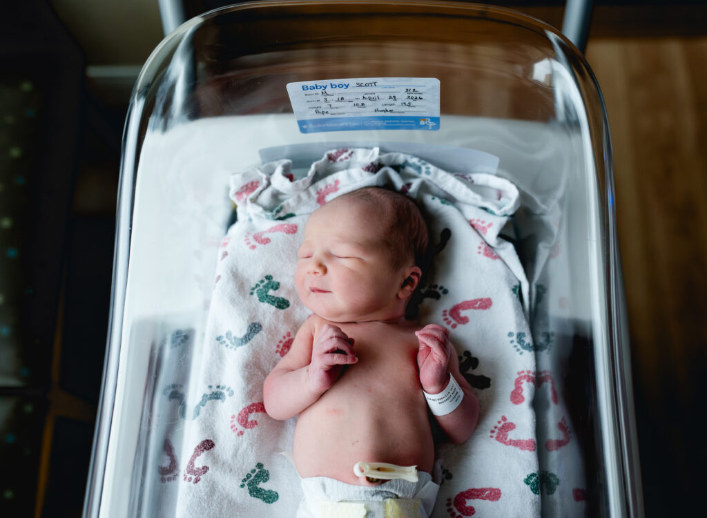 Looking down at a newborn baby in the bassinet in the hospital room, showing the baby's I.D. bracelet.
