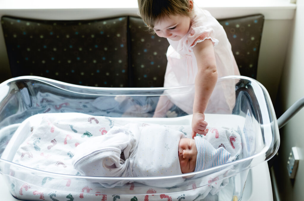 Older sister reaching towards the new baby during the Fresh 48 session in Fort Worth.