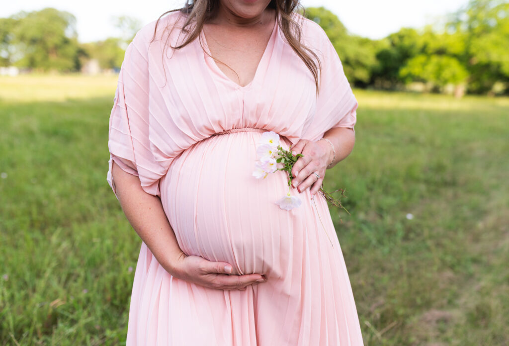 During a first-year collective package session, a mom in a pink dress poses facing forward for her maternity session.
