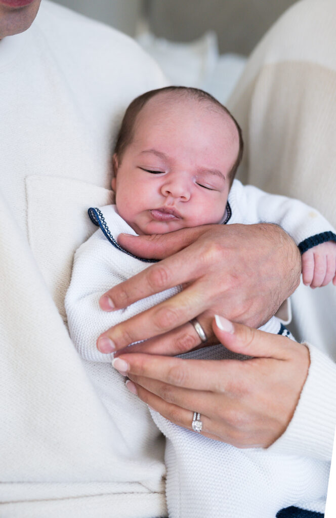 A newborn baby is held by his mom and dad's hands.
