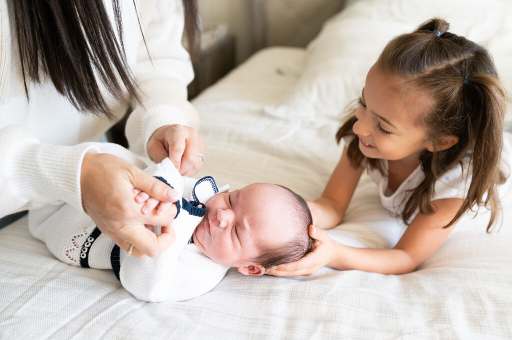 An older sister helps her mom dress her newborn brother for a photo session with Allison Krogness.