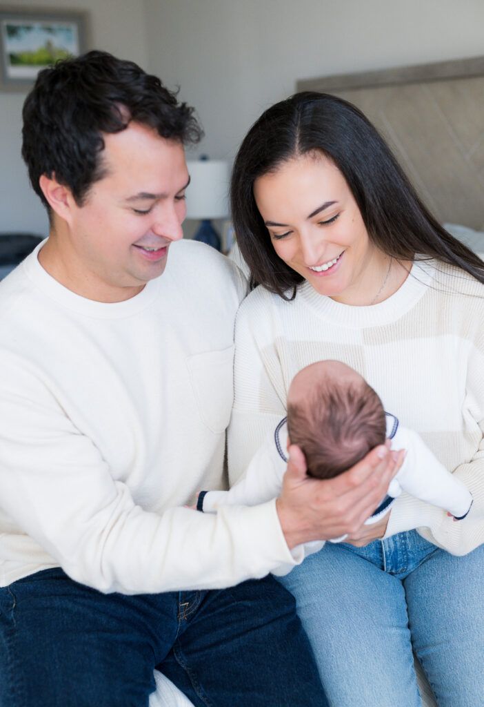 Newborn parents hold their newborn son together and gaze down at him.