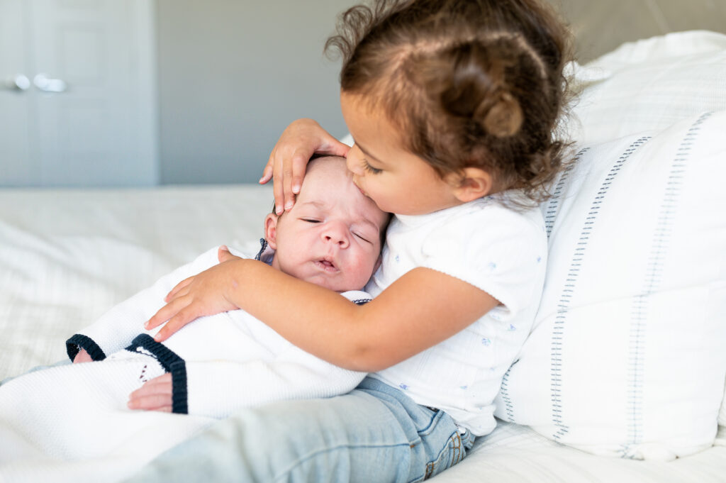 An older sister holds her newborn brother while looking closely at his face.
