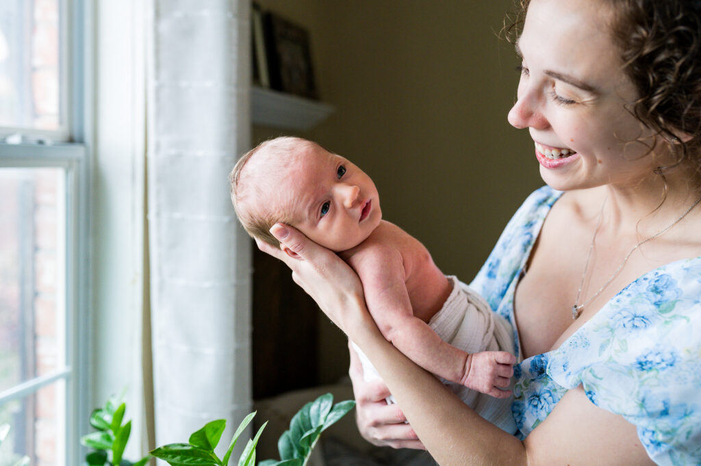 A mom smiles down at her newborn son while posing during a session for her first year collective package.
