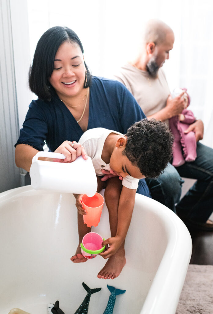 Preparing your toddler for a new baby by telling them they will still have fun, like playing with bath toys together while dad holds the newborn.
