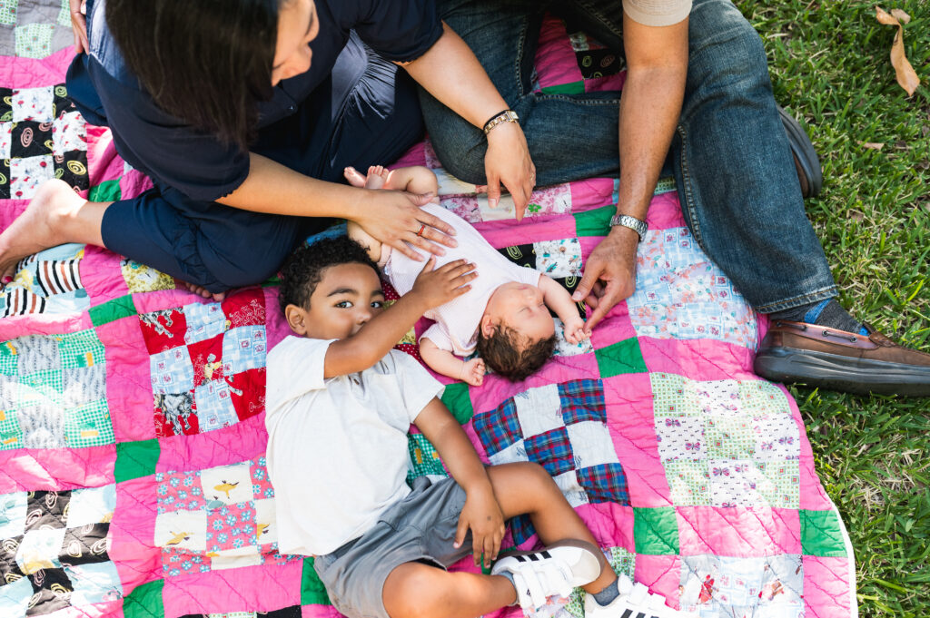 A toddler gently pats his newborn sister during a photo session with Allison Krogness.