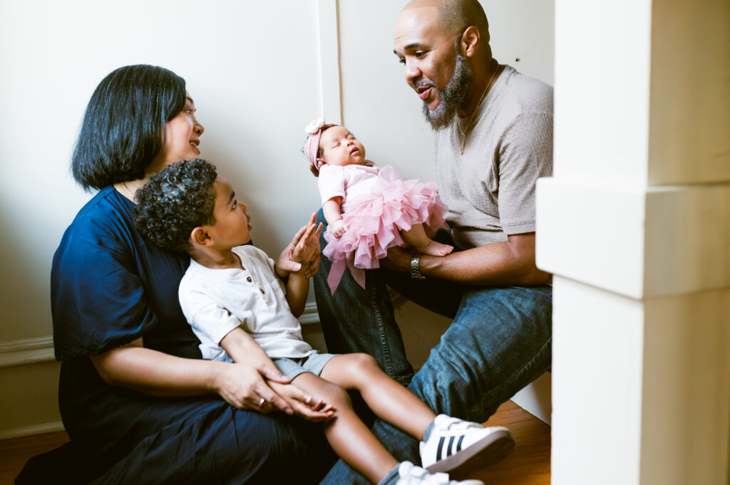 A mom and her toddler look at dad who is holding their newborn daughter during a fort worth newborn session.
