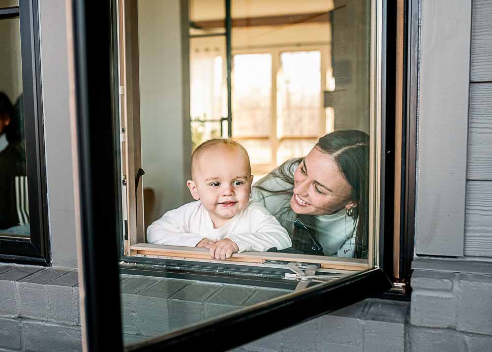 A mom and her infant son are looking out the window during a Fort Worth lifestyle photography session.
