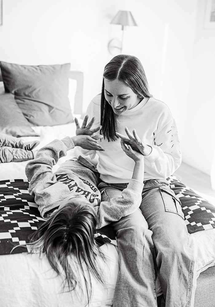 A black and white image of a mom playing with her daughter's hands during a family photography session.
