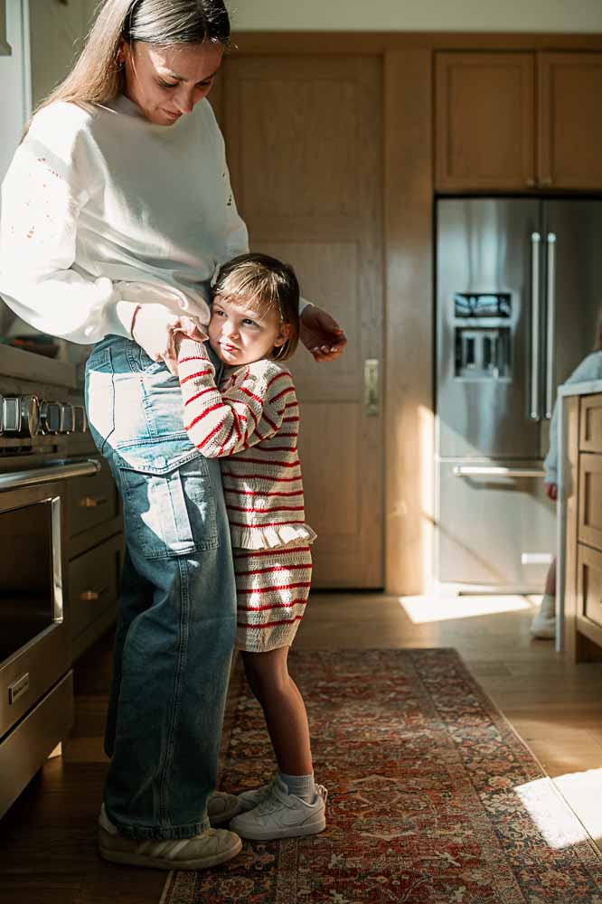 Mom and daughter hug in the kitchen sunlight during an in-home photography session.

