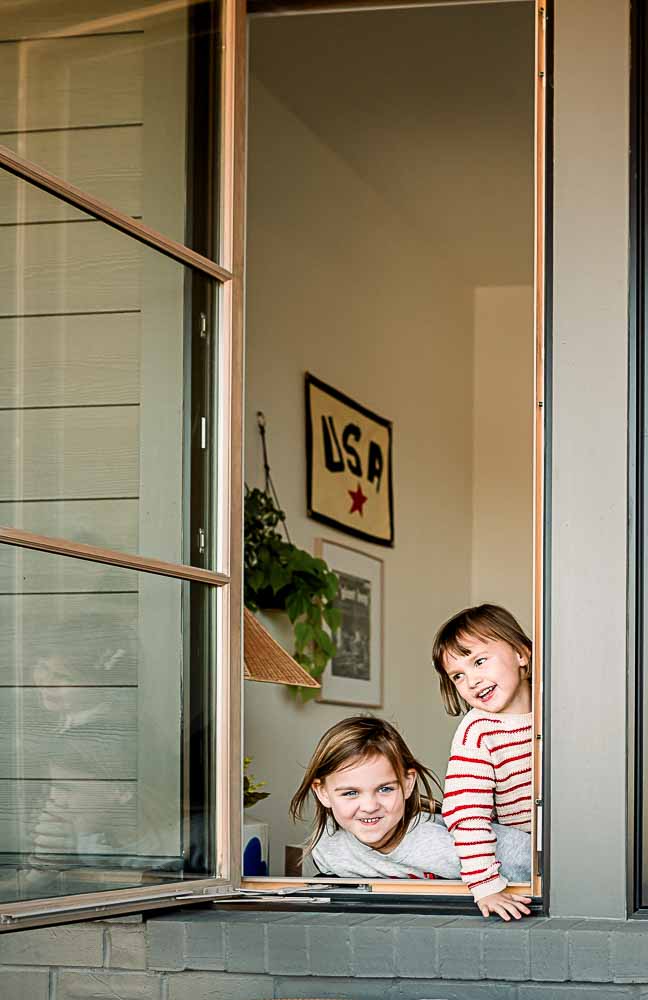 Two sisters are making silly faces while looking out the window during a Fort Worth family photo session.
