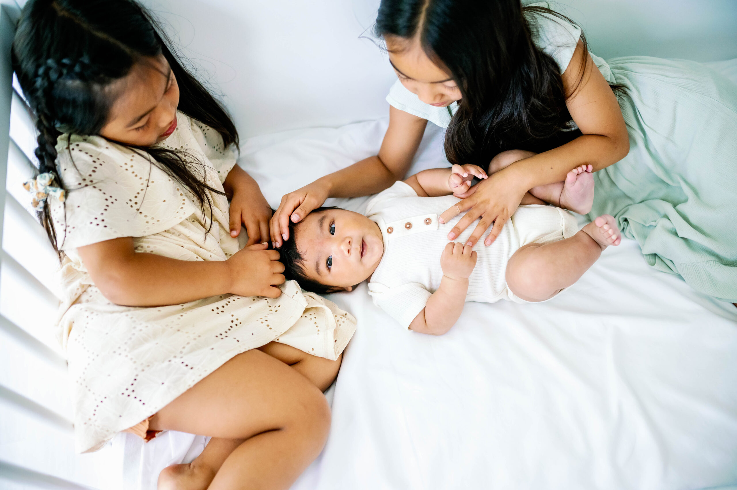 Two older sisters playing with their newborn brother while he lays in a crib